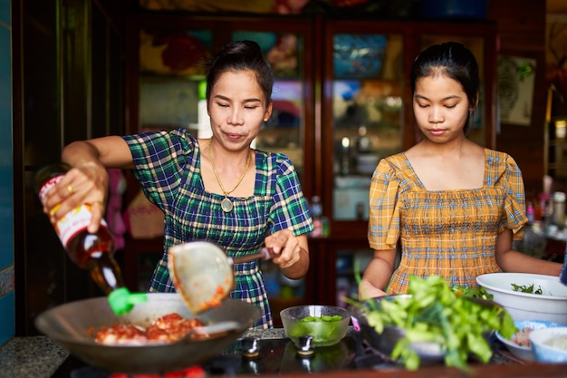 Madre tailandese e figlia che cucinano insieme curry rosso nella cucina domestica tradizionale