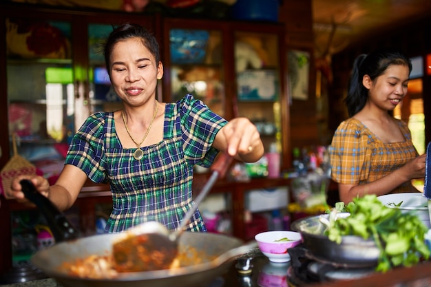 Photo thai mother and daughter cooking together in rustic kitchen making red curry