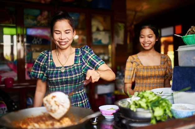 Thai mother and daughter cooking together in rustic kitchen making red curry