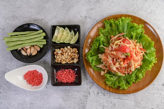 Photo thai papaya salad on salad in a wooden plate with yardlong beans and garlic