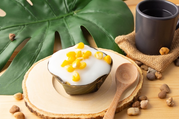 Thai Pudding Kokosnoot top met maïs, Desserts verpakt in bananenbladeren.Thaise mensen noemen "Khanom Tako".Tako met maïs geplaatst op een houten schotel en houten lepel, met thee in zwart glas.