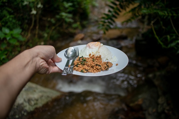 Thai rice topped with stir-fried pork and basil with fried egg on river stream.