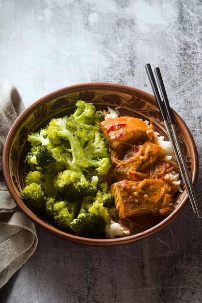 Thai salmon dish in coconut sauce with fresh broccoli and rice in a clay bowl with chopsticks