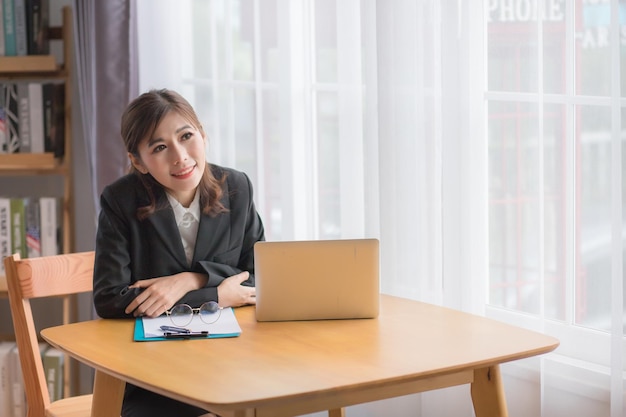 写真 黒のスーツを着て、彼女のオフィスの机に笑みを浮かべてタイの東南アジアの実業家