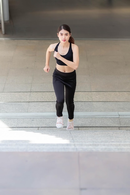 A Thai Southeast Asian woman in black workout clothes running up the stairs.