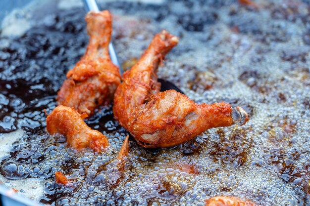 Thai street vendor sells grilled chicken legs meat at street food market in island Koh Phangan, Thailand. Frying chicken legs in a pan close up. Boiling oil in frying pan for cooking