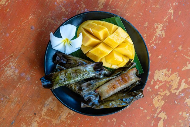 Thai style dessert, yellow mango with banana sticky rice in palm leaves. Yellow mango and sticky rice is popular traditional dessert of Thailand. Close up