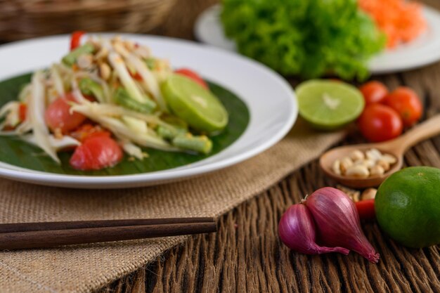 Photo thai style spicy food som tum food concept props decoration garlic lemon peanuts tomatoes and shallots on wood table