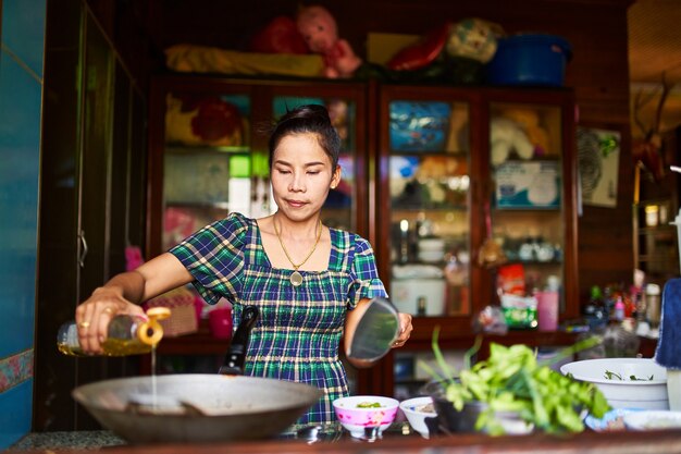 伝統的な家庭の台所で中華鍋に油を注ぐタイの女性