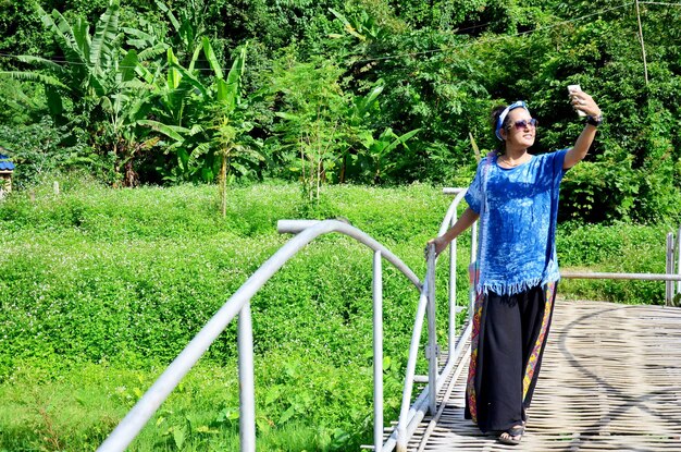 Thai woman use smart phone take photo view of Baan Natong village on wooden bamboo bridge in Phare Thailand