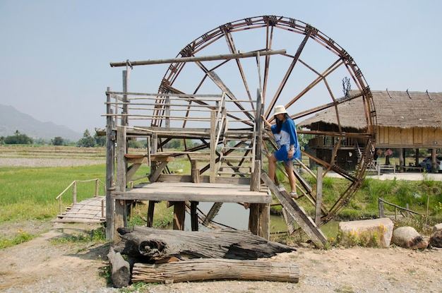 Thai women people travel and posing with big wooden turbine baler water wheel or wood noria water with landscape rice field mountain at Thai Dam Cultural Village in Chiang Khan at Loei Thailand