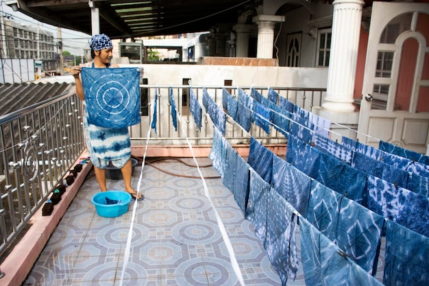 Thai women working Indigenous knowledge of thailand tie batik dyeing indigo color or mauhom color and hanging process dry fabric in the sun at outdoor on top of house in Nonthaburi Thailand