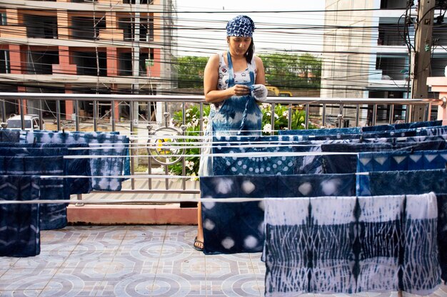 Thai women working Indigenous knowledge of thailand tie batik dyeing indigo color or mauhom color and hanging process dry fabric in the sun at outdoor on top of house in Nonthaburi Thailand