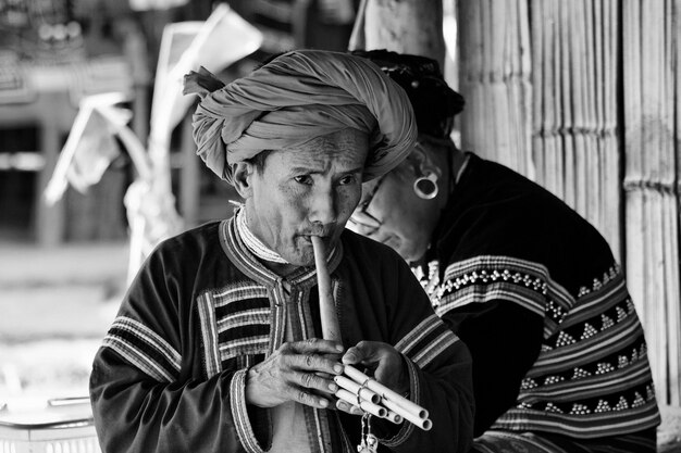 Thailand, Chiang Mai, Karen Long Neck hill tribe village (Kayan Lahwi), Karen man in traditional costumes playing a flute