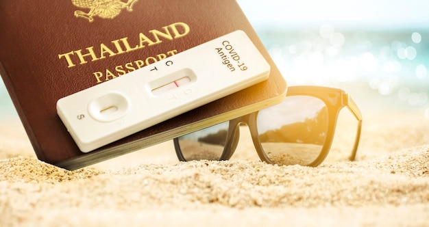 Passaporto thailandese e kit di test dell'antigene covid-19 con risultato del test negativo e occhiali da sole posizionati sulla spiaggia sabbiosa, concetto di vaccinazione del passaporto