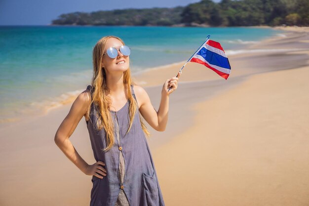 タイはコロナウイルス (COVID-19) による隔離を終えた後観光客に再開しました タイの国旗を掲げてビーチで楽しんでいる幸せな女性アジア旅行を楽しんでいる美しい女の子