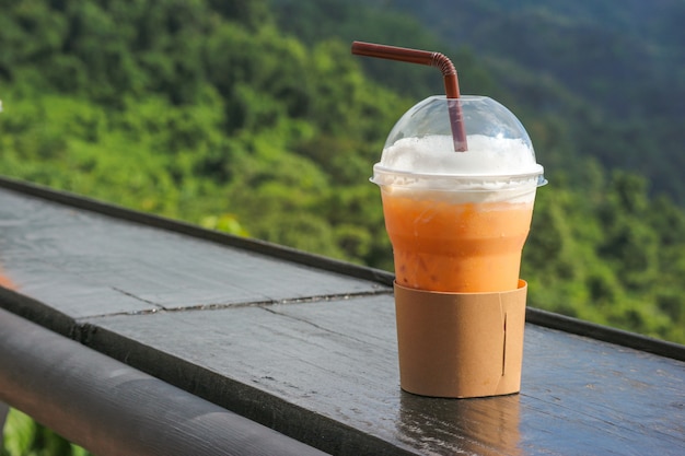 Thaise bevroren thee in plastic beker met natuurlijke weergave als achtergrond.