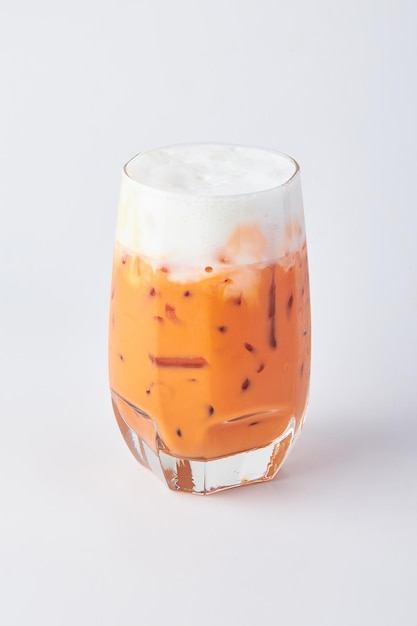 Foto thaise ijstee met melkschuim geserveerd in een helder glas geïsoleerd op een witte achtergrond