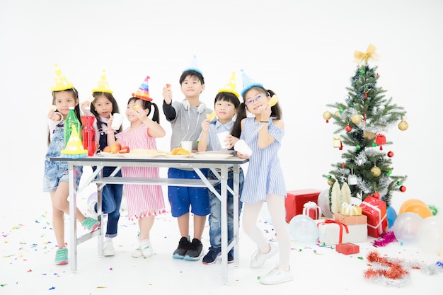 Thaise kinderen uit Chang Asia dragen traditionele kleding en mooie hoeden. Ze dragen snacks op tafel vol met verschillende zoetigheden in een witte kamer gevuld met ballonnen, geschenkdozen en een kerstboom