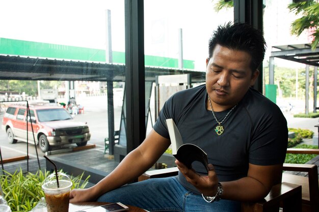 Thaise man zit ontspannen leesboek en praat met ijskoffie drinken in caféwinkel op 13 november 2018 in Saraburi, Thailand