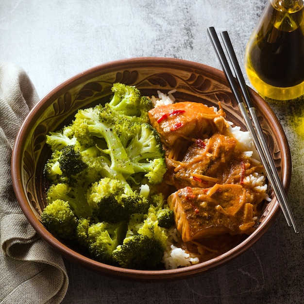 Thaise zalmschotel in kokossaus met verse broccoli en rijst in een kleikom met eetstokjes gezond voedsel met vitamine B5