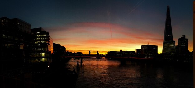 Thames river amidst silhouette buildings against cloudy sky during sunrise