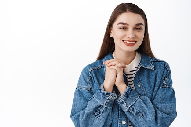 Thank you Smiling cute girl holding hands together and looking pleased and thankful express gratitude feeling delighted standing near copy space for logo banner standing over white background