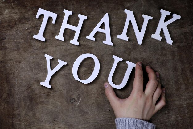 Photo thank you word from white wooden letters on table and hands