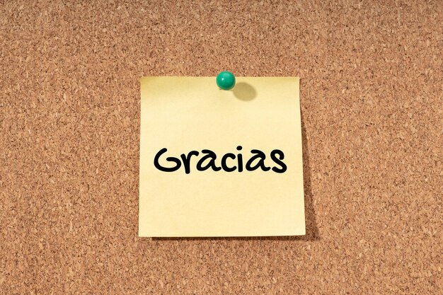 Thanks word in spanish language on yellow note on cork board