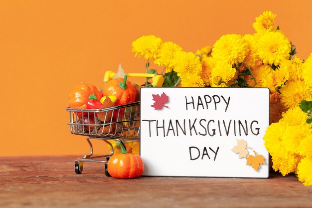 Thanksgiving autumn composition with yellow flower and shopping cart with pumpkins and acorns on orange background. Lightbox with the phrase Happy thanksgiving day. Autumn holidays, fall concept.