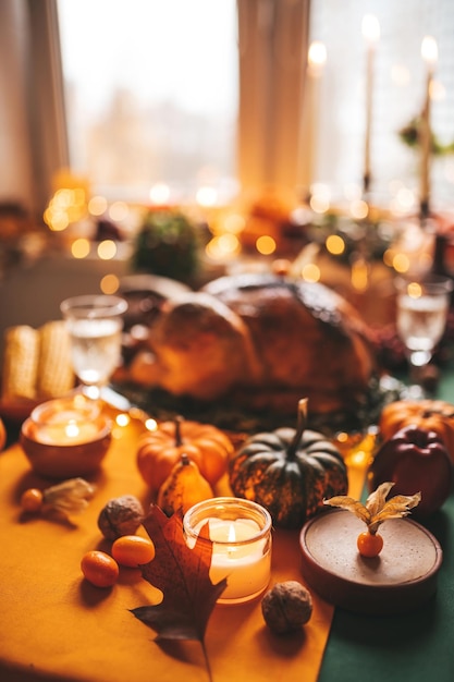 Thanksgiving day dinner with holiday autumn decor and candles family dining room table set with delicious golden roasted turkey on platter garnished rosemary fresh small pumpkins