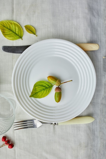 Thanksgiving Day or Halloween dinner table place setting decorative with acorns, leaves on white tablecloth background, view from above, top view, flat lay.