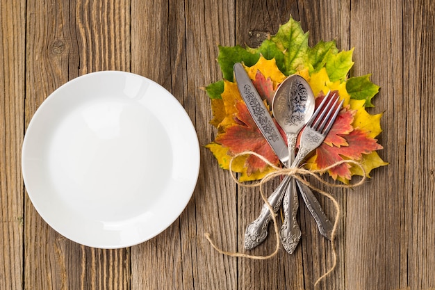 Thanksgiving dinner plate with fork, knife and autumn leaves on rustic wooden table. Top view, copy space