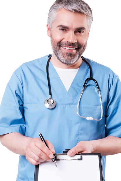 That is what you need! Cheerful mature doctor looking at camera and smiling while pointing copy space on his clipboard and standing isolated on white