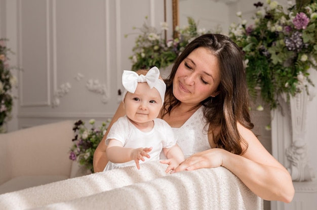 Фото Малышка стоит на диване со своей мамой-брюнеткой и смотрит в камеру счастливое младенчество
