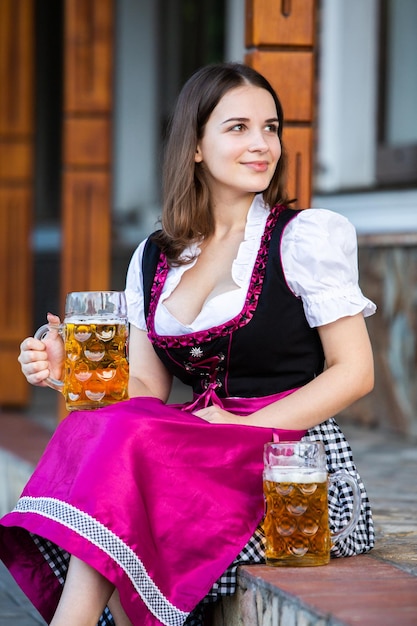 사진 아름다운 갈색의 여성은 독일의 옥토버페스트에서 2 파인트의 맥주를 들고 있습니다.