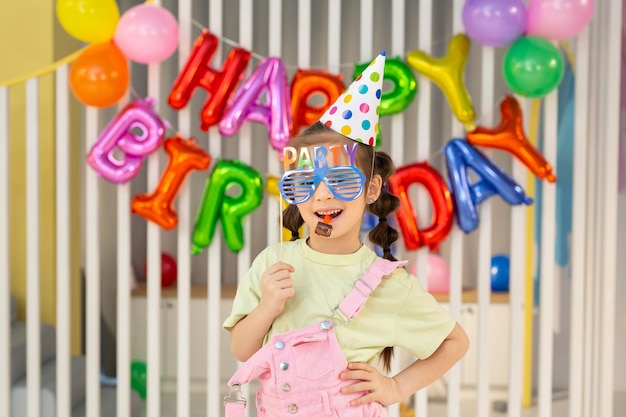 写真 パイプと小道具でお祝いの帽子をかぶった誕生日の女の子が楽しんでいます