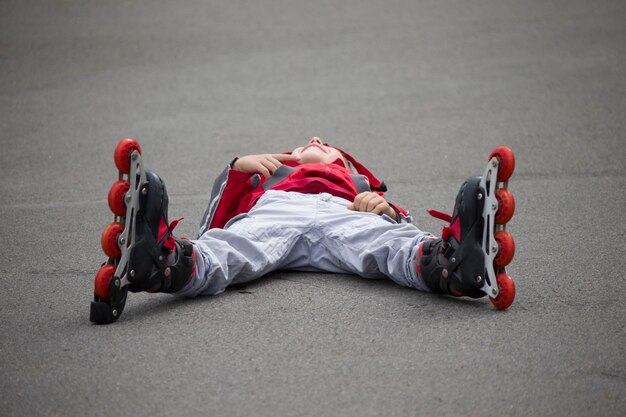 写真 舗装の上に横たわっているローラースケートの少年ローラースケートの子供が倒れた