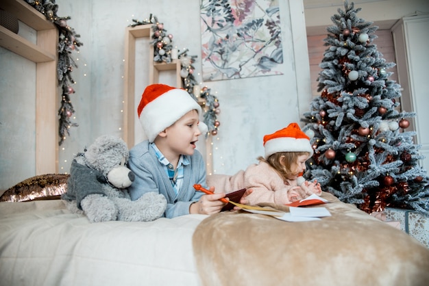 少年はサンタクロースに手紙を書きます。クリスマス家族の夜。新年のプレゼント。装飾された明るいリビングルーム