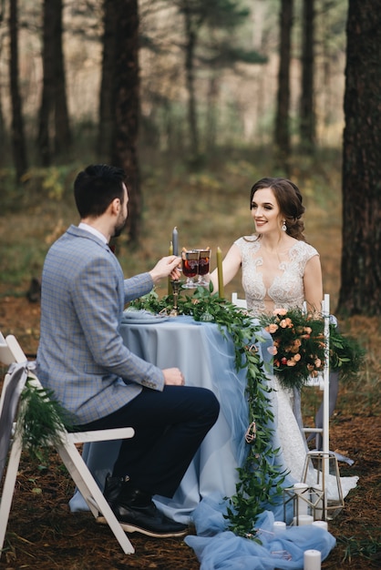 Жених и невеста сидят за столом на двоих в лесу. они улыбаются и пьют глинтвейн. осень. концепция романтического свидания