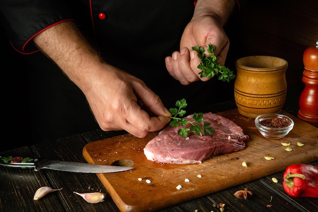写真 シェフはバーベキューの夕食のために生牛肉のステーキにパセリを加え,香りのあるローズマリーとスパイスでキッチンテーブルの作業環境を調整します.