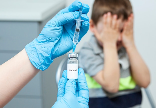 子供は注射を恐れています。予防接種が怖かったので、少年は顔を手で覆った