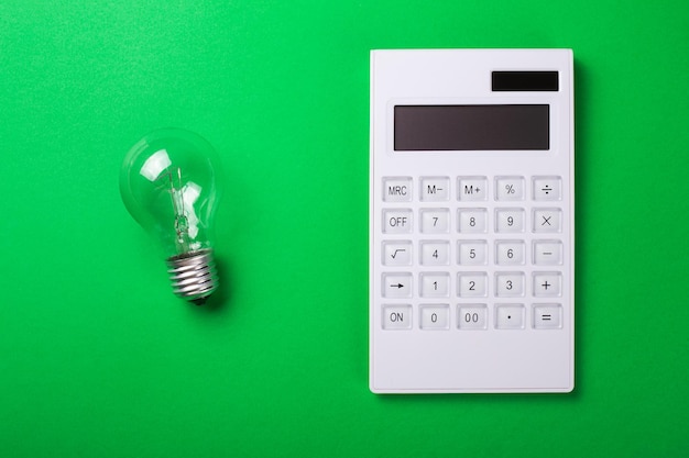 Фото Концепция экономии электроэнергии сокращение оплаты счетов за коммунальные услуги калькулятор с лампой накаливания эдисона и лампочка led на зеленом фоне