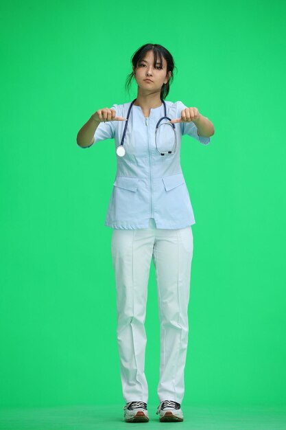 写真 緑色の背景の医師の女の子が全身で親指を下に示しています
