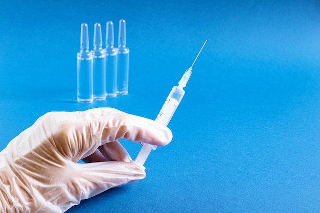 Фото Врачи в белых перчатках держат шприц из флакона с вакциной на синем фоне концепция плановой вакцинации