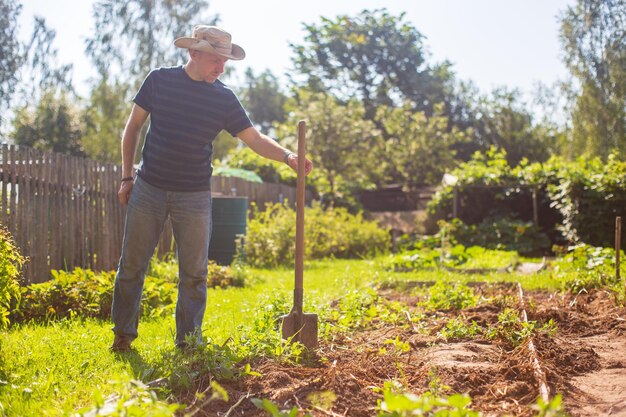 사진 농부 는 정원 에서 <unk> 을 들고 서서 채소 를 심기 위해 토양 을 준비 하고 있다.