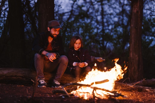 Фото Отец и его сын сидят на бревнах в лесу и жарят зефир на огне