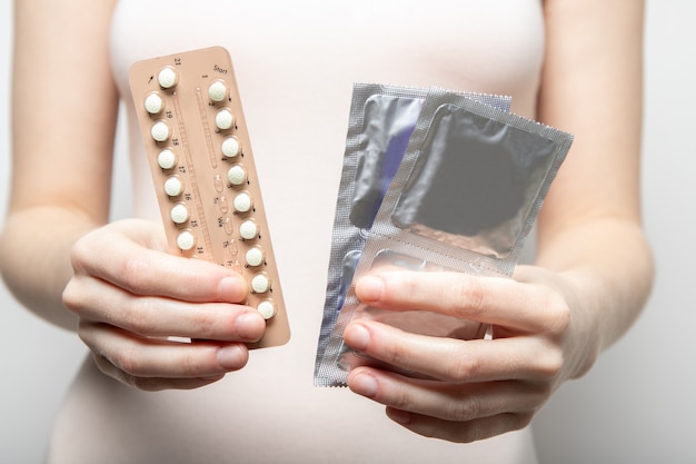 Фото Девушка держит в руках противозачаточные таблетки и презервативы. контрацепция