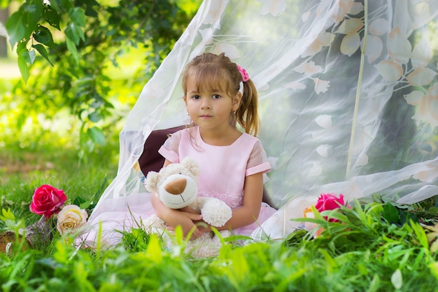 Девушка в элегантном платье сидит с мишкой в палатке на свежем воздухе