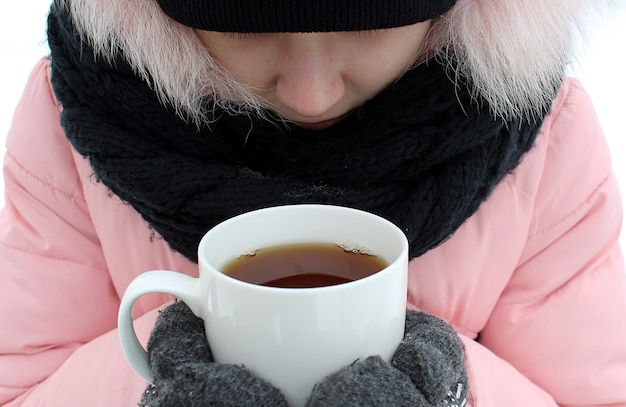 写真 女の子は寒くて、暖かく保つために熱いお茶を一杯持っています。冬の凍るような日。ジャケットとミトンを暖かく着て、スカーフに包まれた男。